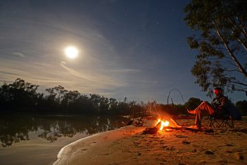 A man sits beside a campfire.