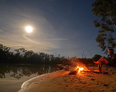 A man sits beside a campfire.