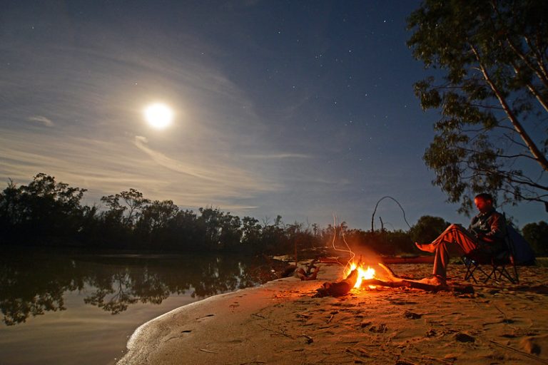 A man sits beside a campfire.