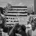 A protester at a No Kings march holds up a poster that is made to look like it is on fire that says "Democracy is burning."