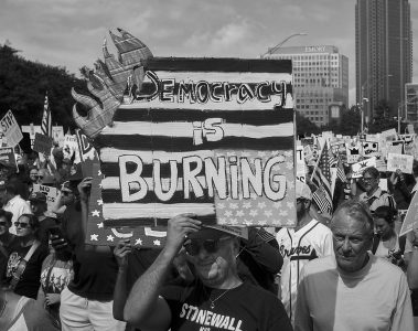 A protester at a No Kings march holds up a poster that is made to look like it is on fire that says "Democracy is burning."